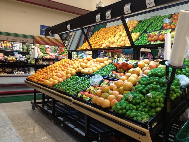 Exhibidores horizontales que contienen cajas de plástico con frutas y verduras en supermercado.