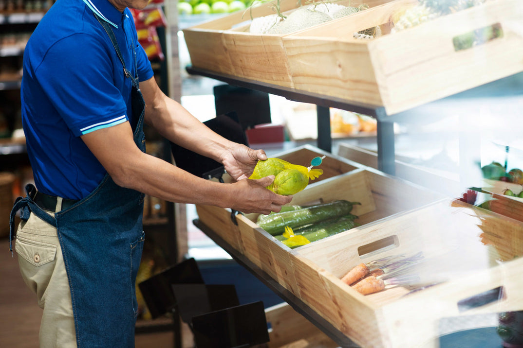 Trabajador organiza calabacitas y zanahorias en cajas de plástico Wood look, orientadas a la conservación de frutas y verduras en punto de venta.